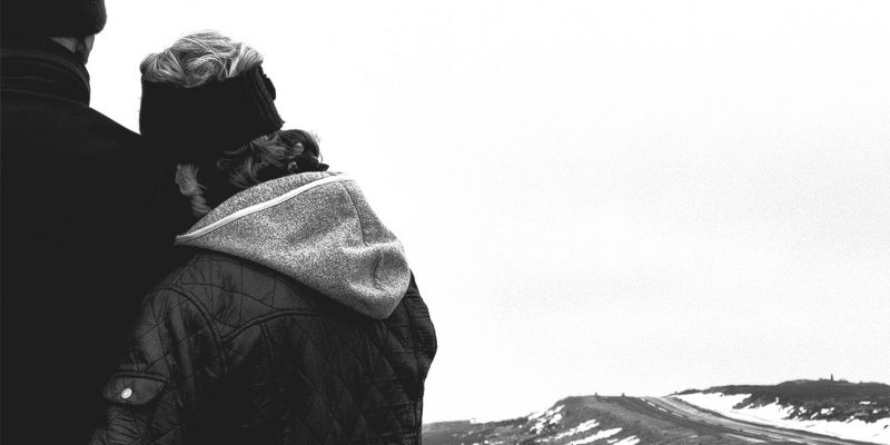 Photograph in black and white showing a couple in the countryside looking at the winding road in the distance