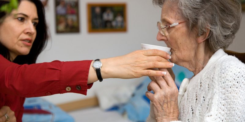 A lady helping and encouraging an elderly lady to drink