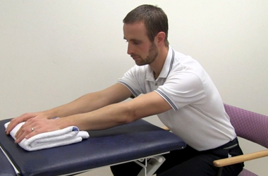 Leaning forward, sliding the towel forward as far as possible