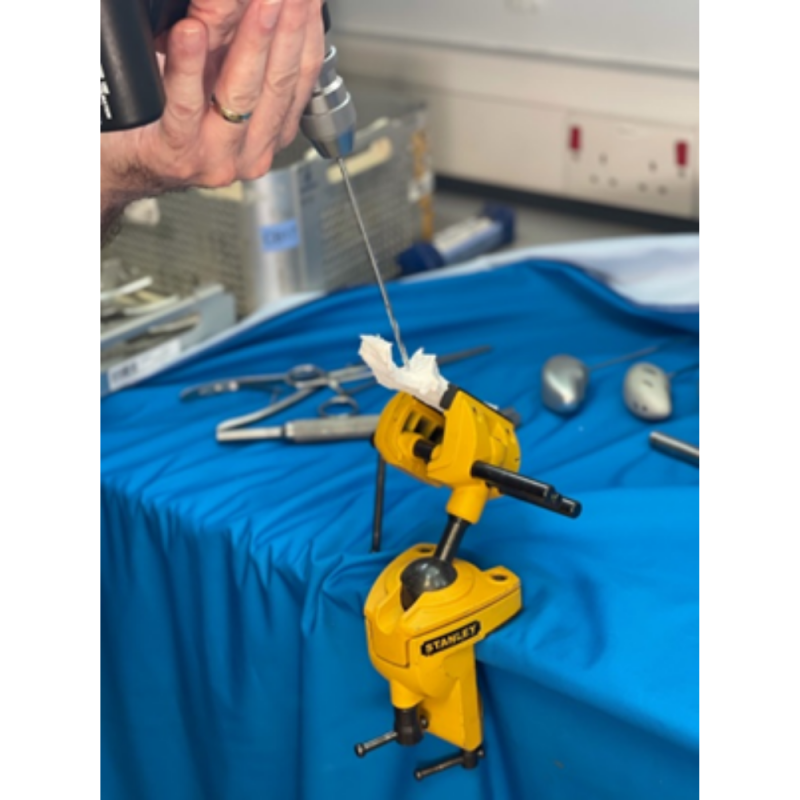 A yellow vice gripping a 3D modelled joint attached to a table with a blue cover. Someone is drilling a hole into the modelled joint.