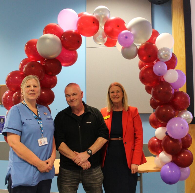 Three people standing in front of a celebration balloon arch
