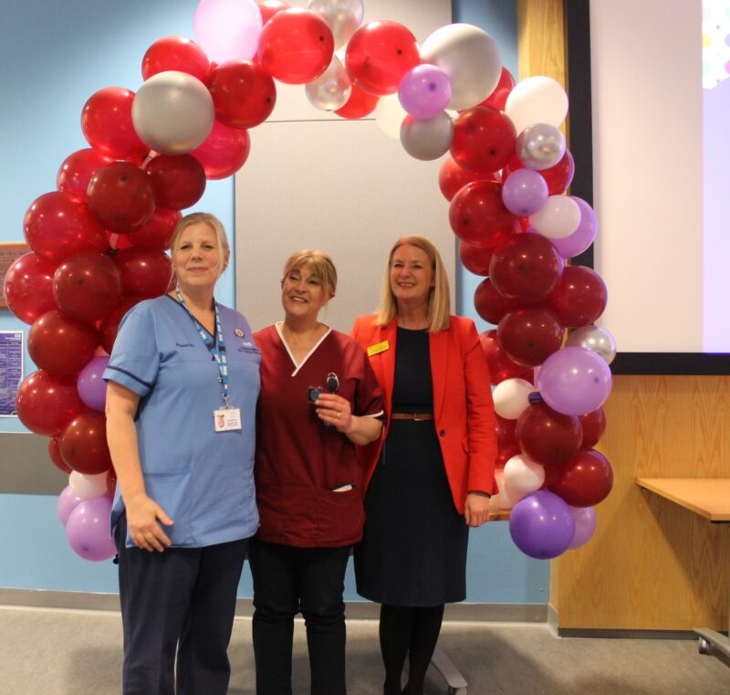 Three ladies standing in front of a celebration balloon arch