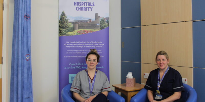 Two ladies sitting on chairs next to a banner and table